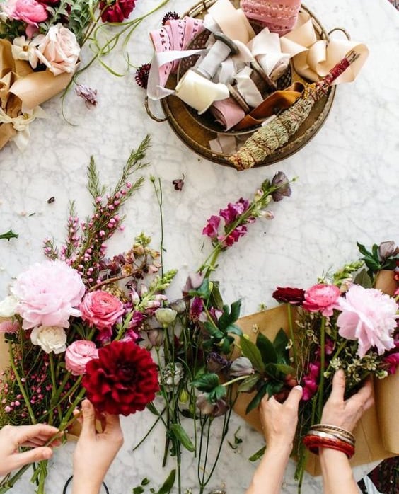 Manos creando una guirnalda floral con rosas y dalias.