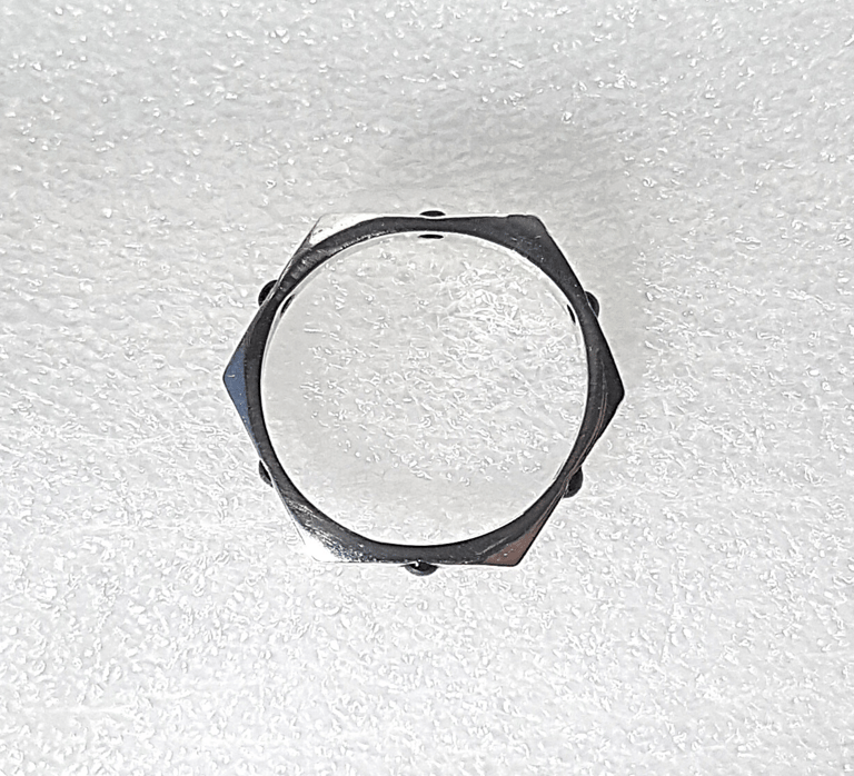A hexagonal sterling silver ring, featuring six small black gemstones, sits on a white textured surface.