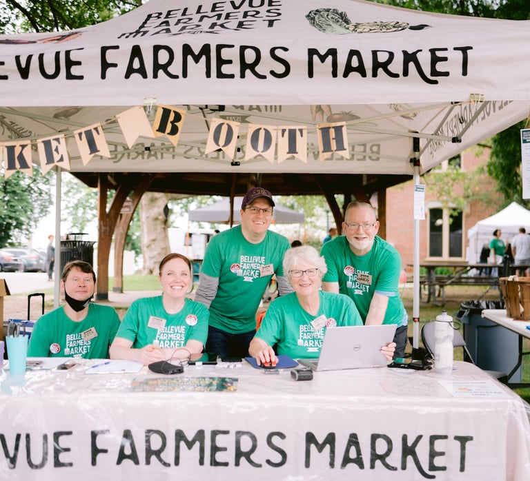 Volunteers smile from behind the Bellevue Farmers Market information booth.