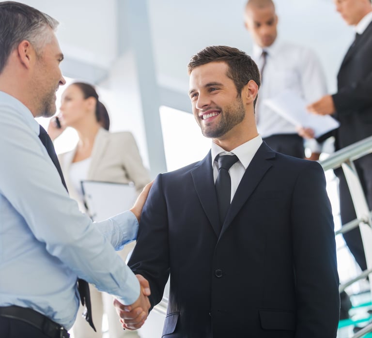 Two smiling businessmen in suits shaking hands in a professional office setting.