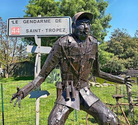 A metal sculpture of Le Gendarme de Saint-Tropez standing next to a French road sign.