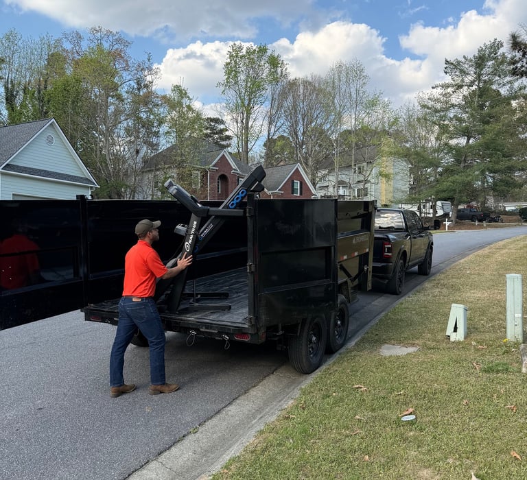 A worker loads a black dumps trailer on a residential street for junk removal services.
