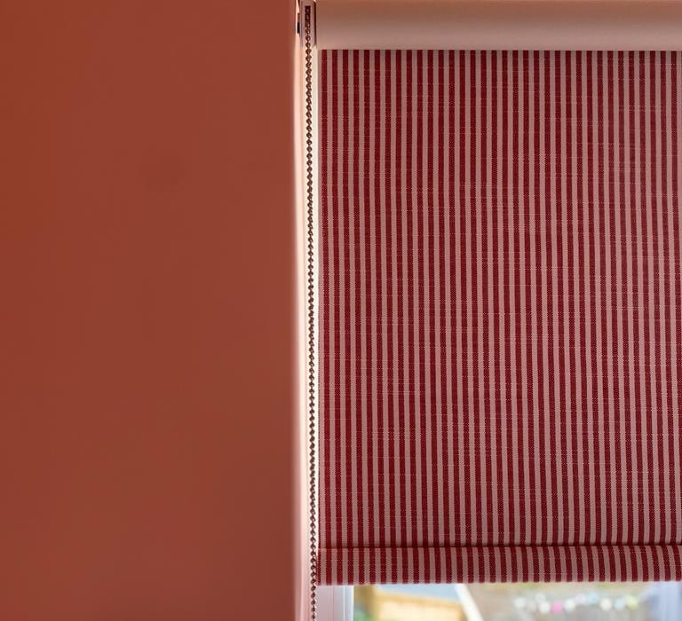 coral pink walls and striped red roller blinds creating a fun yet mature bedroom