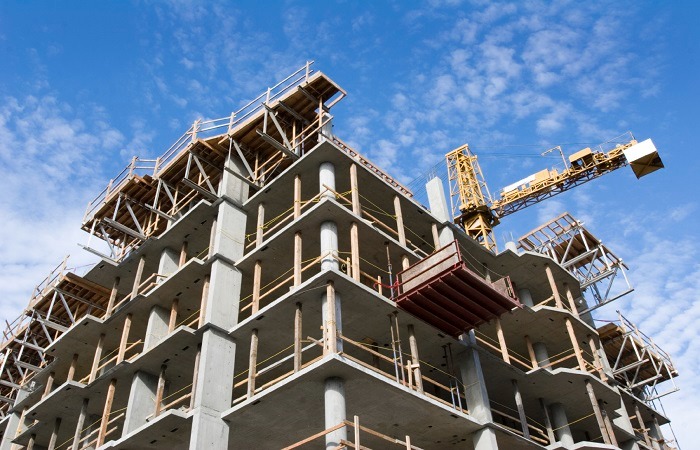 A high-rise concrete building under construction with a yellow tower crane against a blue sky.