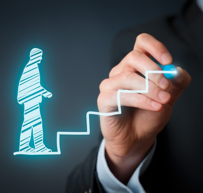 Person drawing a glowing silhouette of a figure climbing stairs, symbolizing progress and growth.