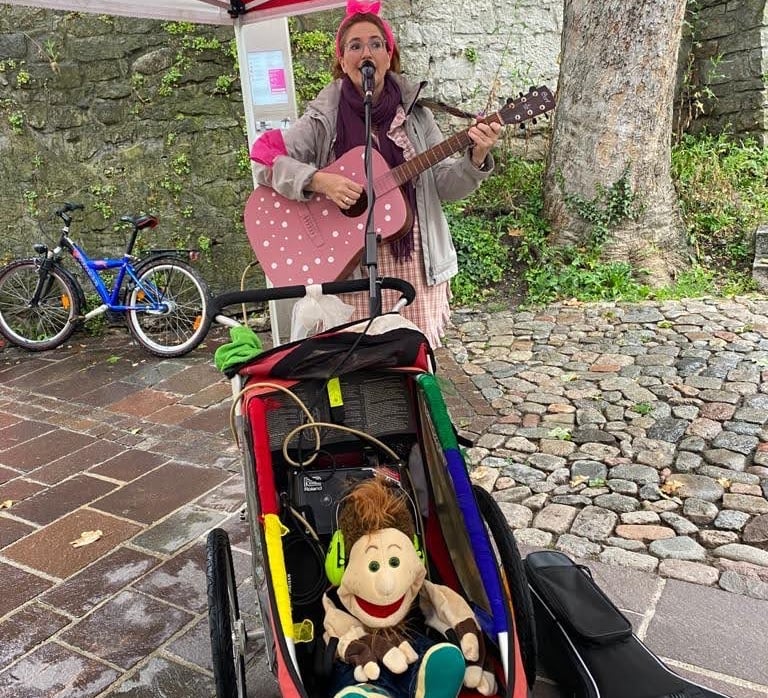 Sängerin Betti mit rosa Gitarre und Kinderwagen in der Tiengener Altstadt. Handpuppe sitzt im Wagen.