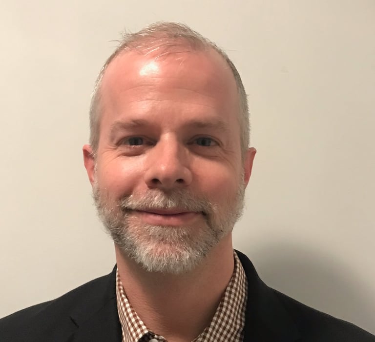 Alexander Slagg with grey beard, black sport coat, checkered button down shirt