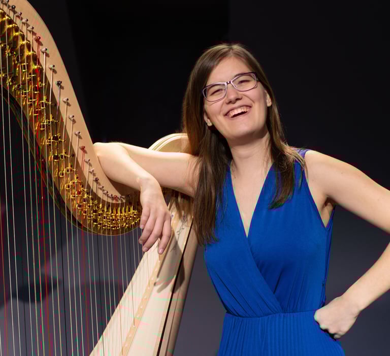 Clara Busemann steht lachen an einer Konzertharfe und hat einen Arm locker über ihre harfe gelegt
