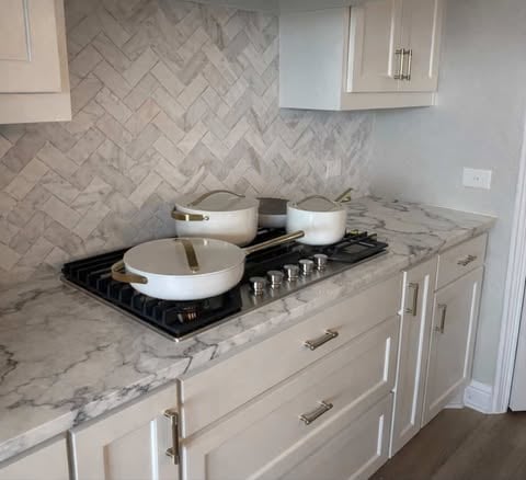 White Caraway cookware set on gas stove with marble countertop and herringbone backsplash