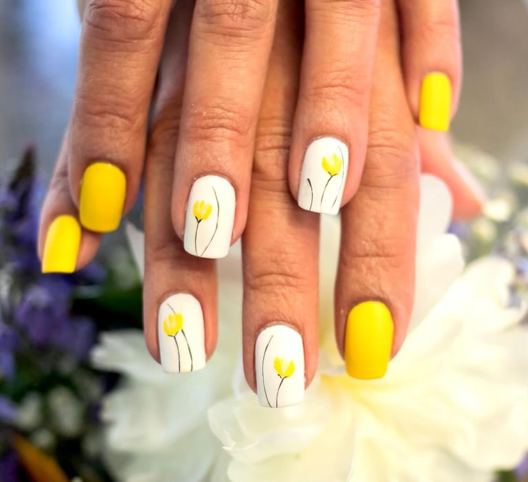 Yellow and white spring manicure with hand-painted floral nail art on white accent nails.