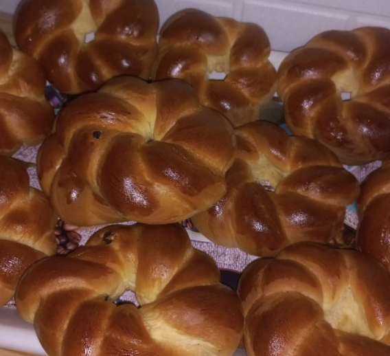 A batch of golden brown freshly baked braided brioche rolls on a cooling rack.