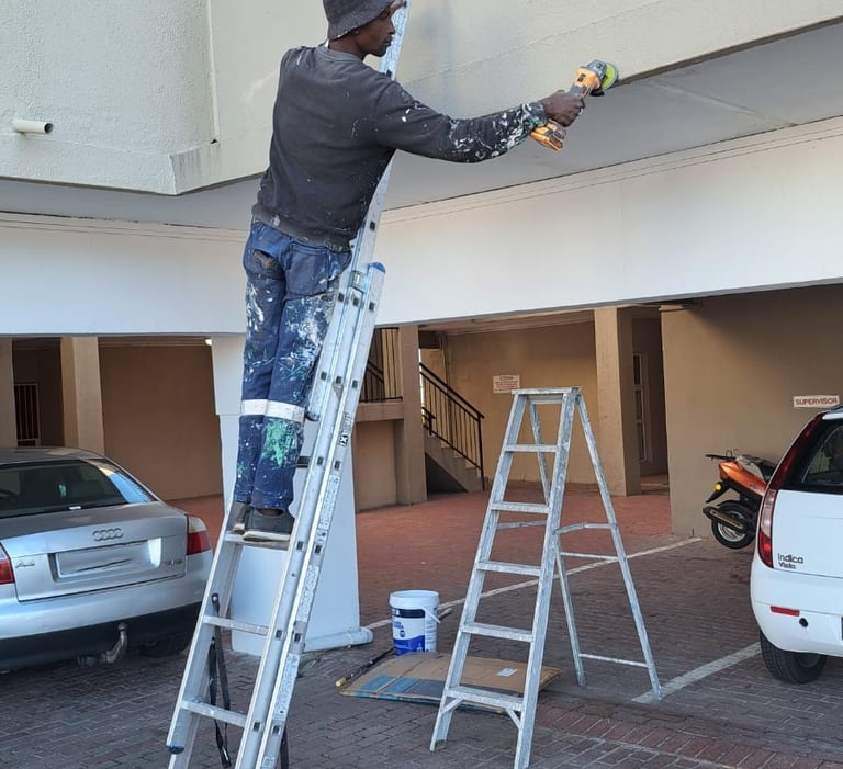 Professional painter on a tall extension ladder painting the exterior facade of a residential building.