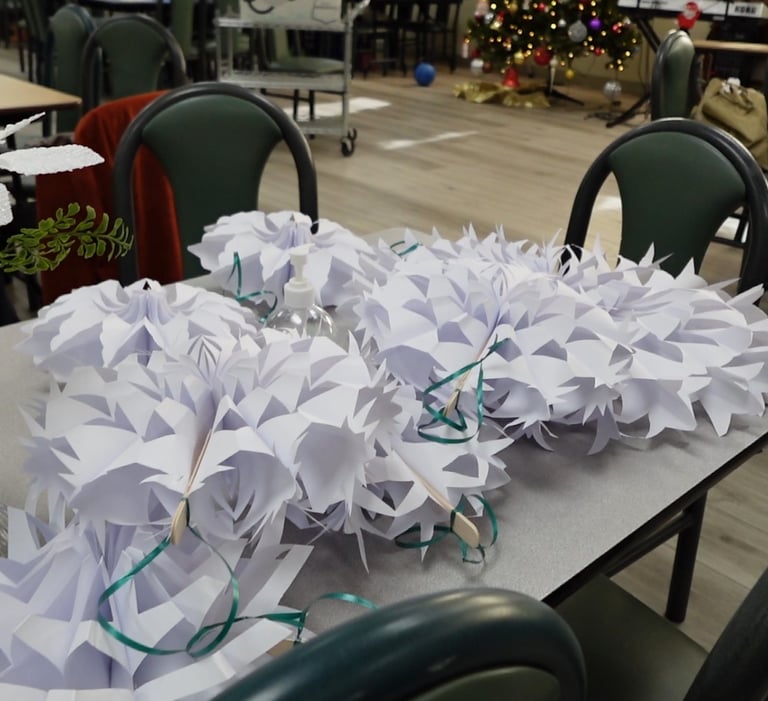 Handmade white paper snowflakes and Christmas decorations on a community center table.