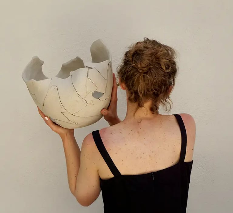 La artista ceramista Claire Lippmann sosteniendo una de sus esculturas a espaldas de la cámara.