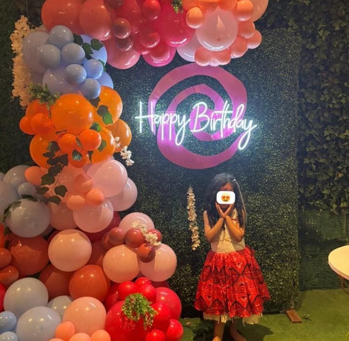 Niña posando en una fiesta de cumpleaños temática de Moana, con letrero de neón ‘Happy Birthday’