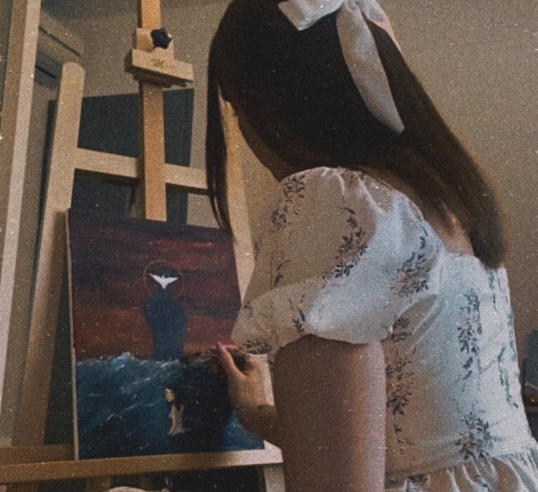 Une jeune femme dans une robe blanche avec un noeud blanc dans les cheveux en train de peindre