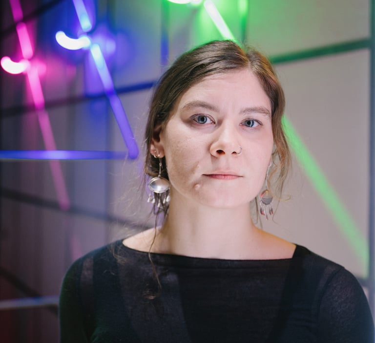 Das Portrait einer jungen Frau, die gerade in die Kamera schaut. Im Hintergrund bunte Lampen.