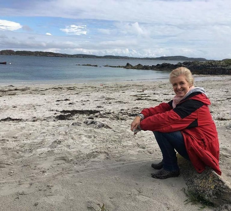 blonde haired woman sitting on a white sandy and rocky coastline bay
