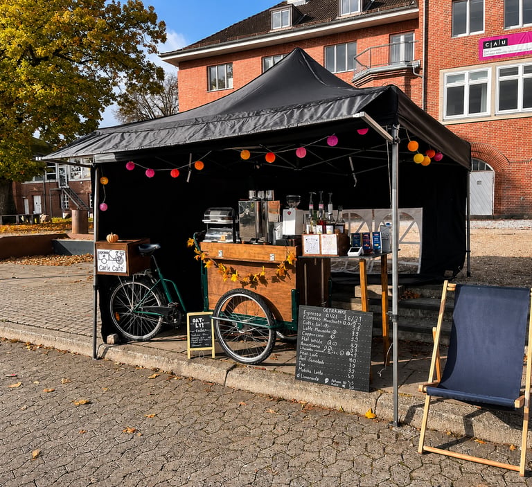 Schwarzes Eventzelt mit Kaffeefahrrad, Kreidetafel-Menü und Lichterkette.