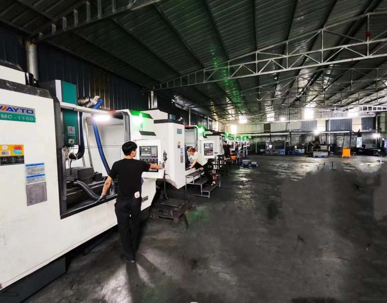 Operators working with a row of industrial CNC milling machines in a large metal manufacturing facility.