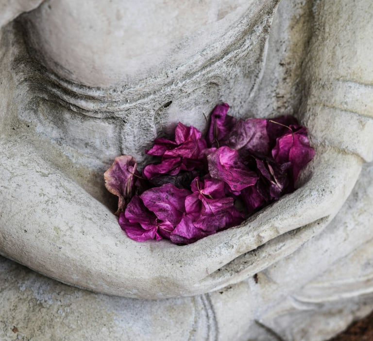 Purple dried flower petals resting in the cupped hands of a stone Buddha statue.