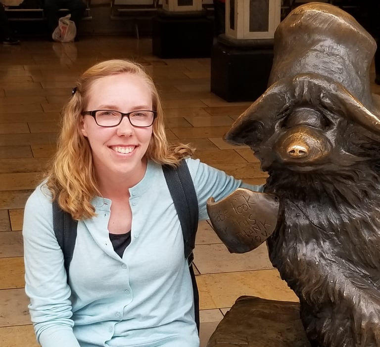 Sarah Schedler, editor for indie authors, poses for a photo next to a statue of Paddington Bear.