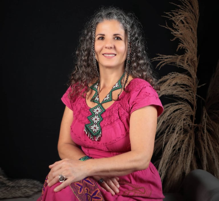 Zsofia, founder of Brevard Massage and Sound Therapy, in a pink folk dress seated by soft reeds