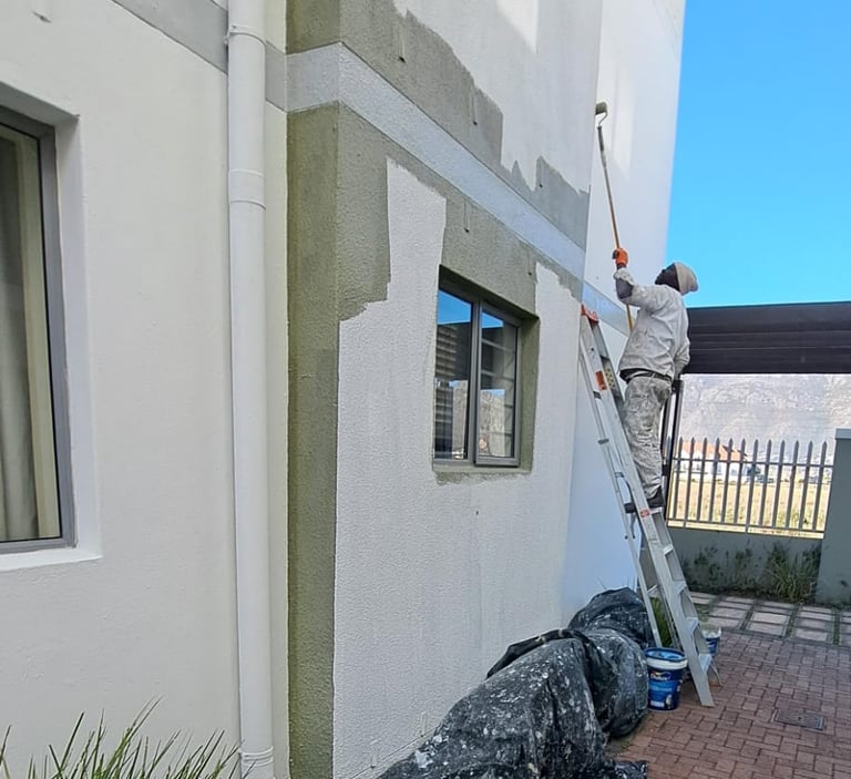 Professional painter applying white exterior paint to a multi-story building using a roller and ladder.