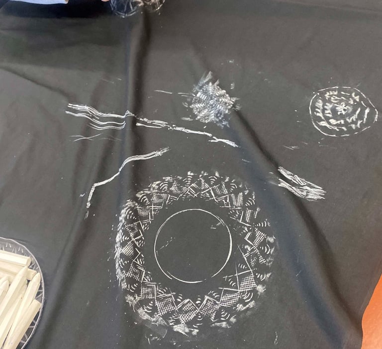 A young person using a stick of chalk on fabric to rub the outlines of a shape underneath the fabric.