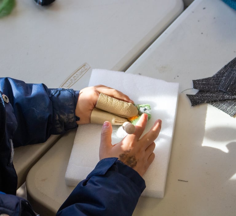 Young child's hands with finger coverings, poking pieces of wool to create a felted creature.