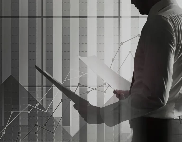 Um empresário analisando relatórios financeiros com gráficos e tabelas de dados ao fundo.