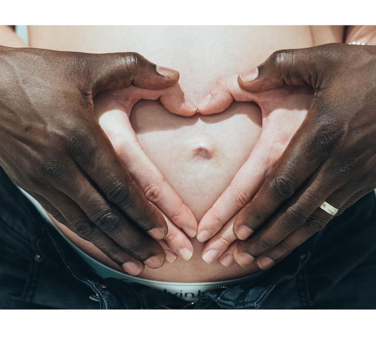 mains d'un ouple interracial sur le ventre de la femme enceinte et formant un cœur