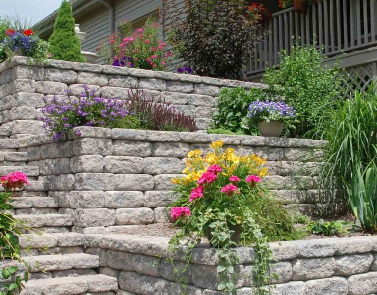 Landscaped block retaining wall with stone steps and plants