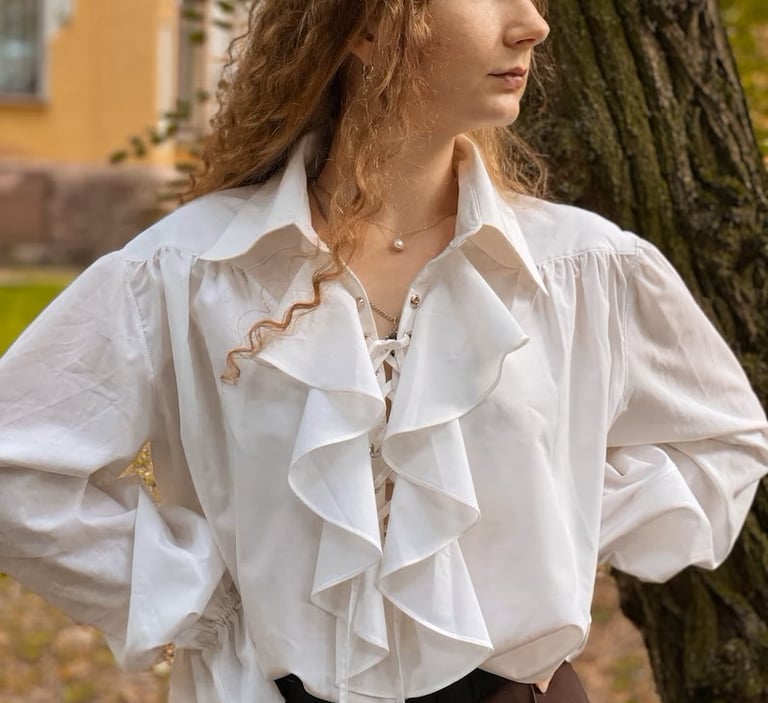 A woman with red-blonde hair wearing a white poet shirt, with a large collar and ruffled front.