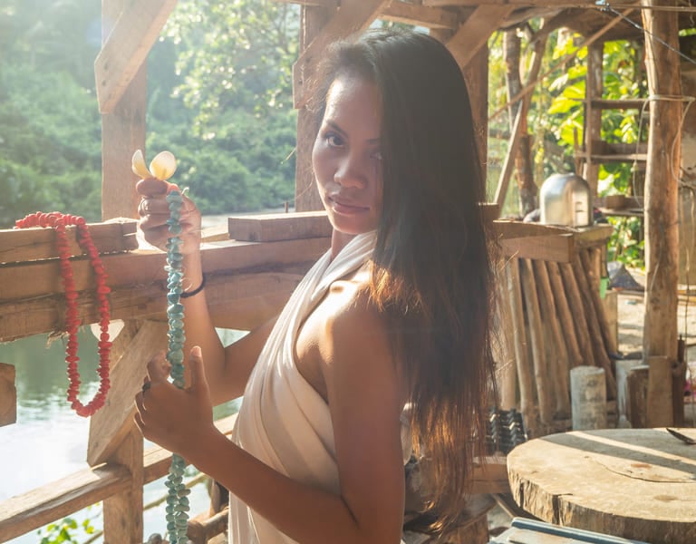 Eine philippinische Frau in einem weißen Kleid hält Perlenketten in einer rustikalen Holzhütte