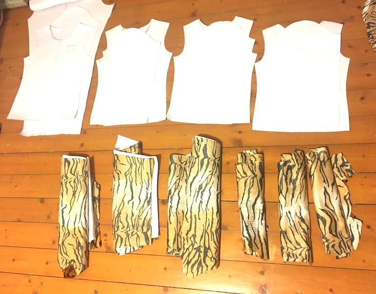White paper sewing patterns and rolls of tiger print fabric laid out on a wooden floor.
