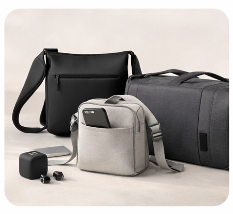 Minimalist grey shoulder bag with a smartphone in the pocket next to a black messenger bag and travel duffel.