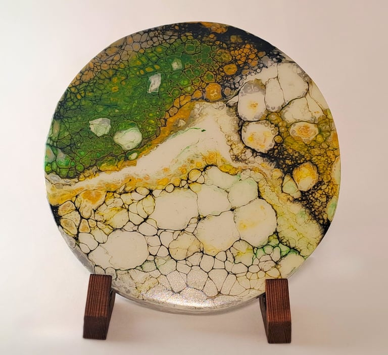 Handcrafted round acrylic pour art piece with green and gold cell patterns on a wooden display stand