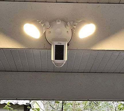 Ring floodlight security camera with dual LED lights installed on a white soffit for home surveillance.