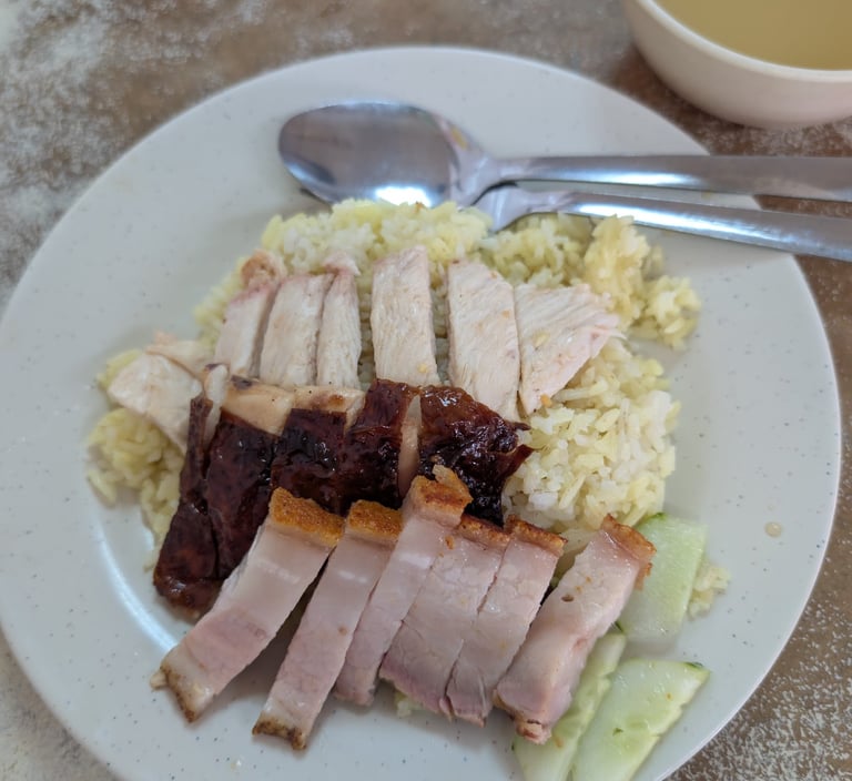 boiled chicken rice plate with roasted pork belly, char siu, and cucumber slices.