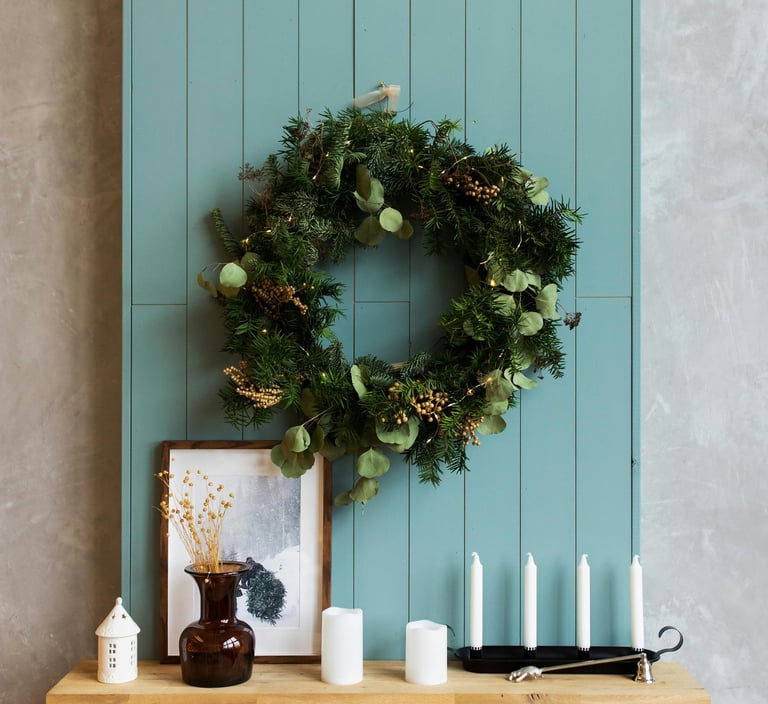Elegant Christmas wreath made of eucalyptus and pine with bow hanging around a fireplace mantel.
