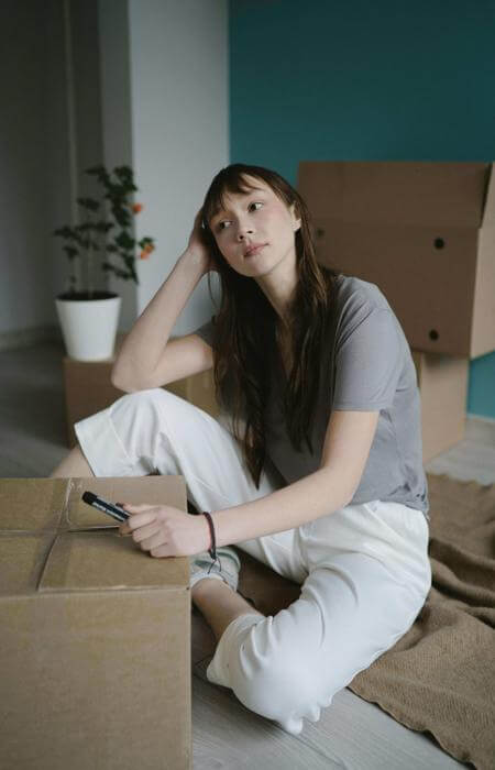 a woman sitting on a cardboard box with a cell phone, wondering