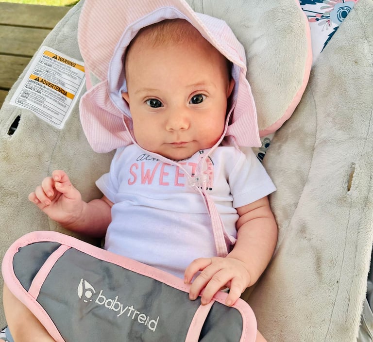 A newborn baby girl with a pink sunhat sitting in a bouncer, looking at the camera