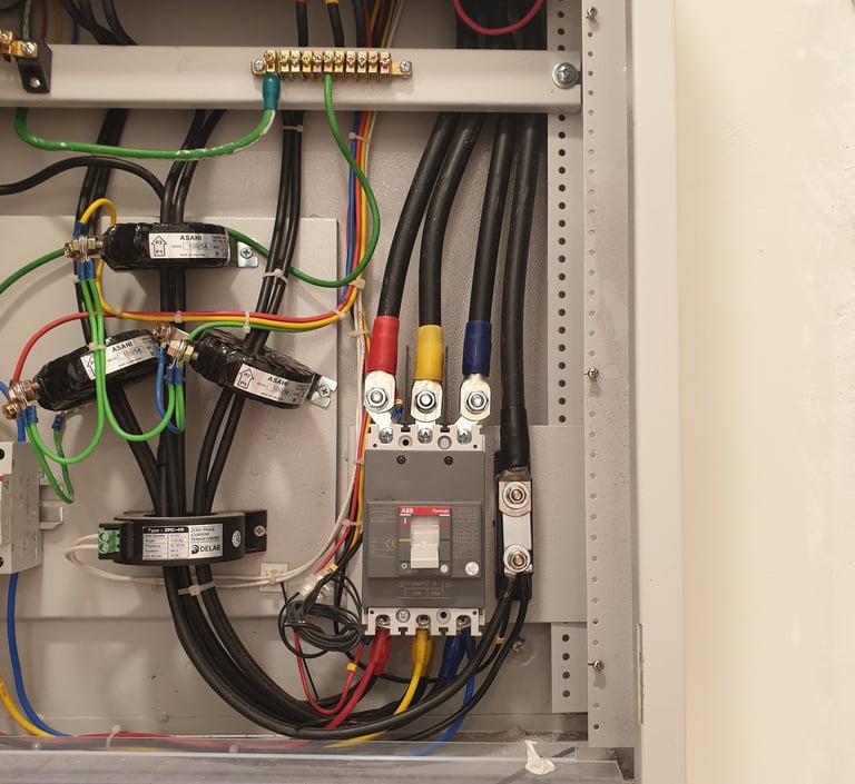 Industrial electrical panel with ABB circuit breaker, current transformers, and colored wiring for power distribution.