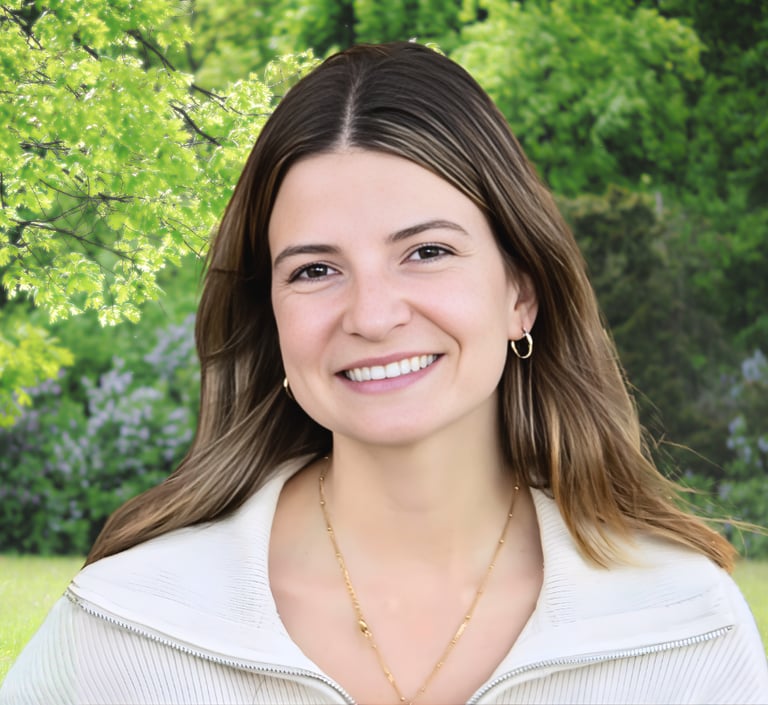 Smiling woman with light brown hair wearing a white sweater in a sunny green park setting.