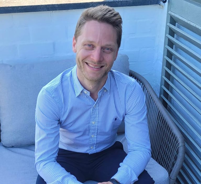 Photo de Stéphane Marquis vétu d'une chemise et d'une pantalon assis sur un fauteuil à l'extérieur