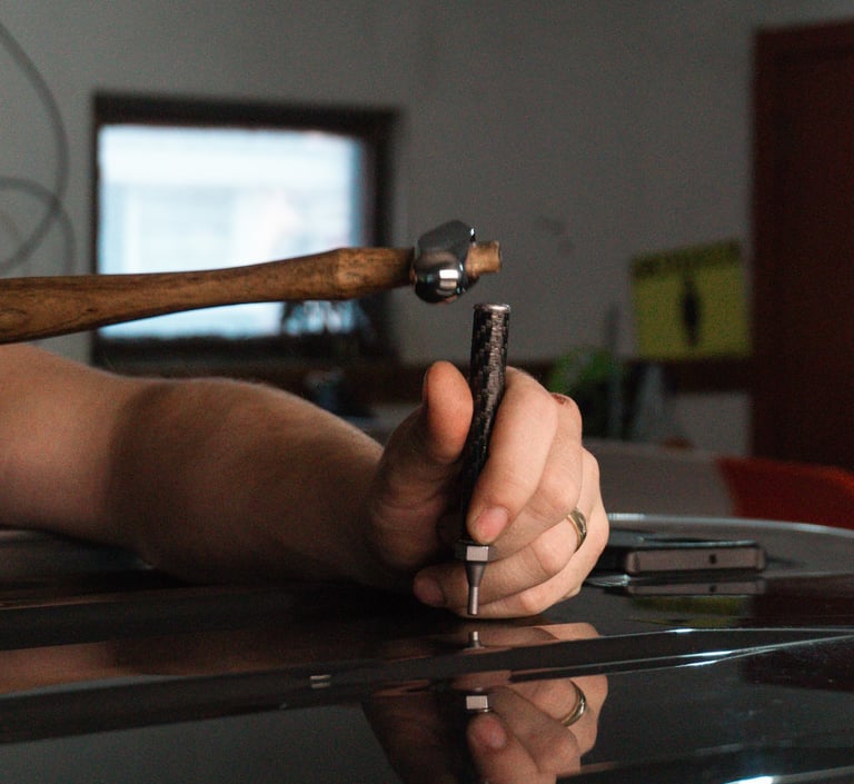 Professional technician using a hammer and punch tool for paintless dent repair on a black car.
