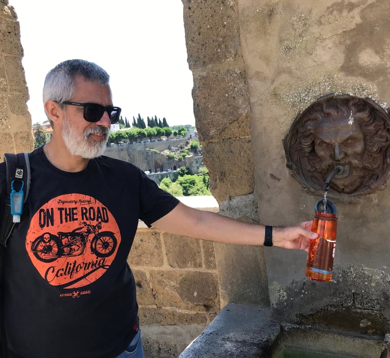 Uma pessoa de óculos escuros pegando água em uma antiga fonte na Itália