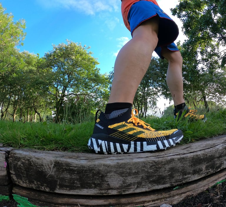 a person standing on a log in the woods weating adidas trainers