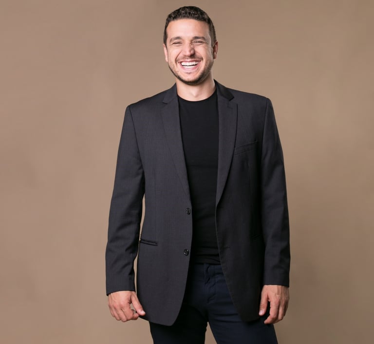 Smiling professional man in a black blazer and t-shirt posing for a corporate headshot.